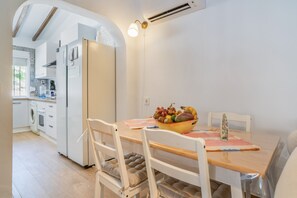 Un coin repas avec une table en bois, des chaises blanches et un saladier rempli de fruits.