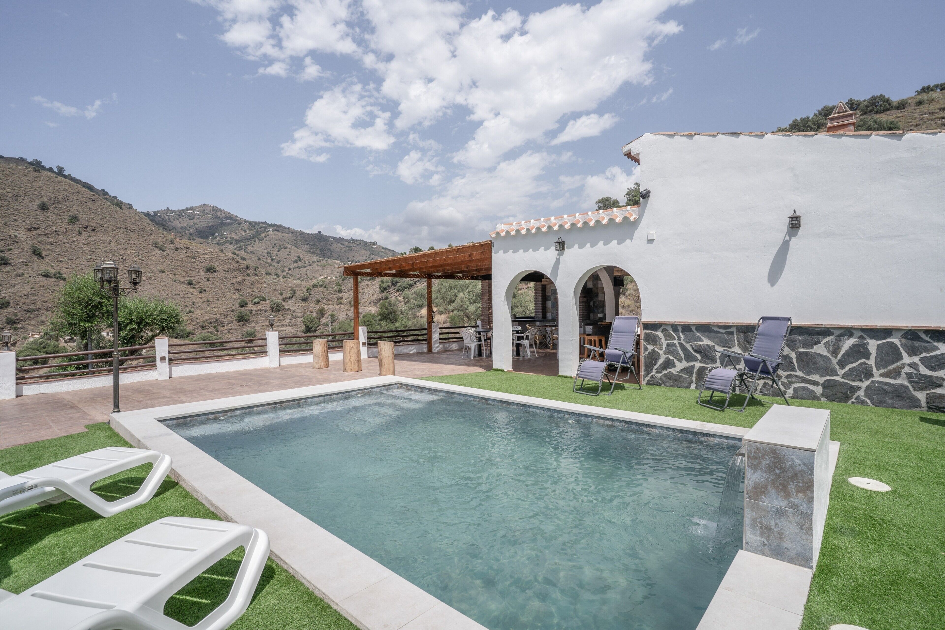 Ein Swimmingpool mit einer Pergola und Sitzbereich im Freien, umgeben von einer gebirgigen Landschaft.