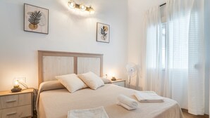 Un lit bien fait, avec des oreillers et des serviettes pliées, une table de chevet avec une lampe et un luminaire fixé au mur.