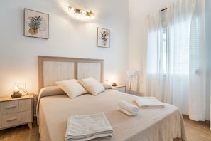 Ein ordentlich bezogenes Bett mit Kissen und gefalteten Handtüchern, ein Nachttisch mit Lampe sowie eine Wandleuchte.