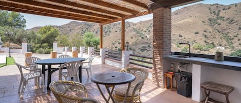 Une terrasse extérieure avec des tables et des chaises, un mur de briques et une vue sur un paysage vallonné.