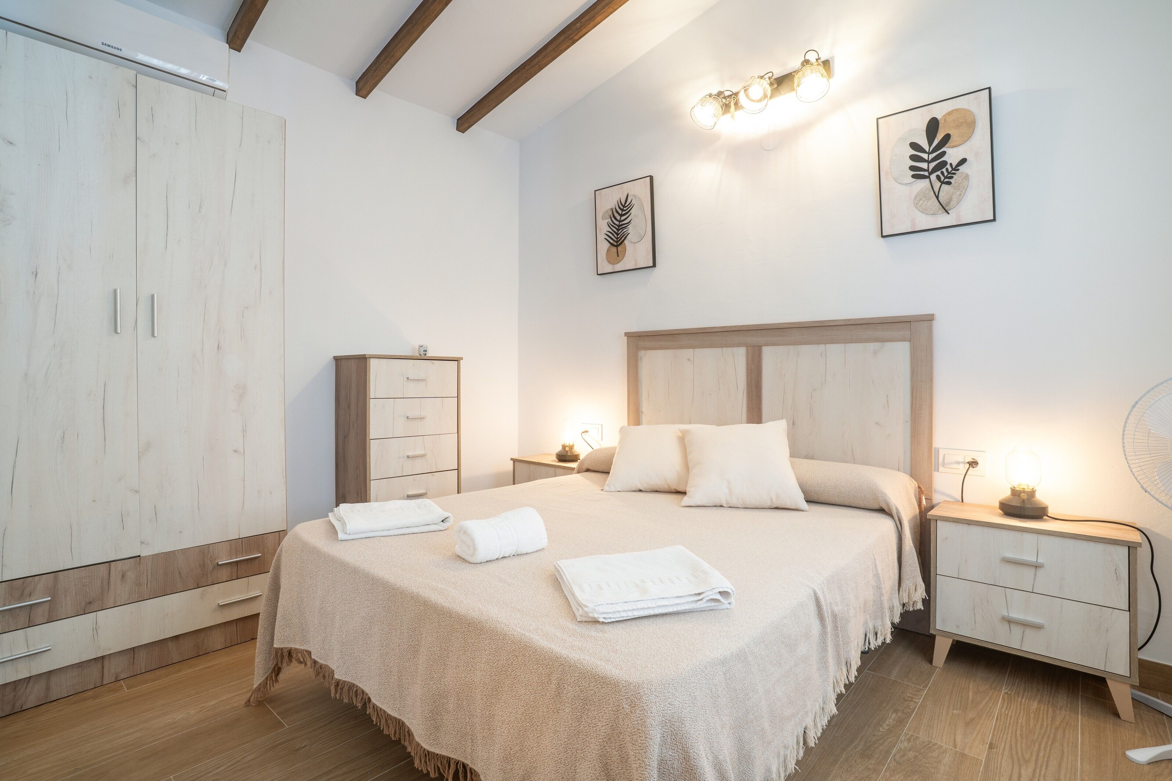 A bedroom with a bed, bedside tables, a wardrobe, and artwork on the walls.