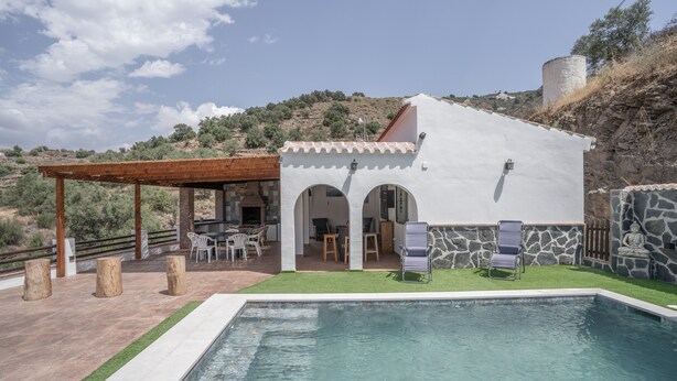 Une villa avec piscine, un espace salon extérieur et un mur en pierre.