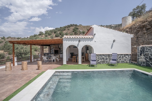 Eine Villa mit Swimmingpool, Sitzgelegenheiten im Freien und einer Steinmauer.