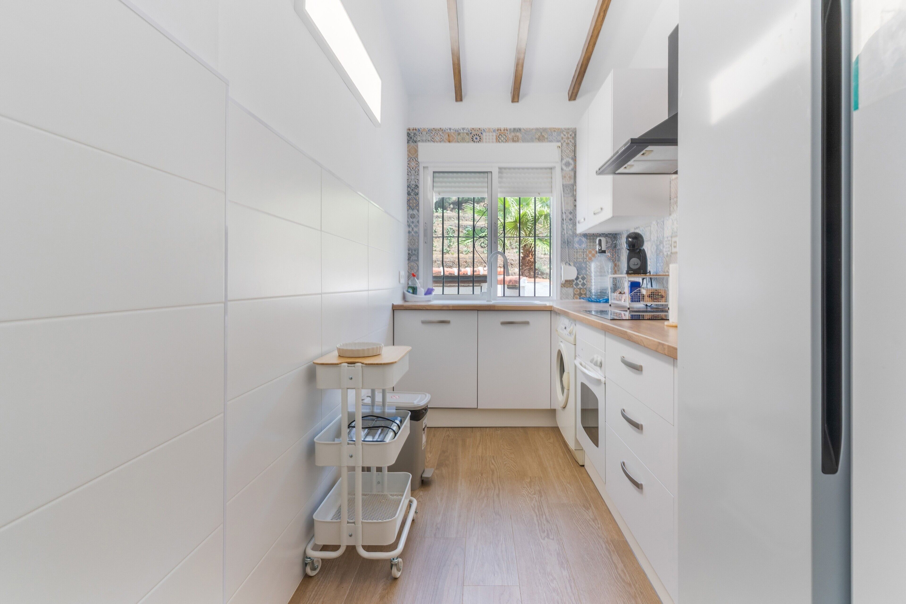 A compact kitchen with white cabinetry, a wooden countertop, a built-in oven, and a window with a view of greenery.