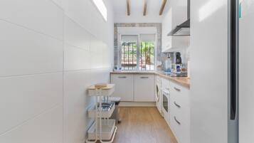 A compact kitchen with white cabinetry, a wooden countertop, a built-in oven, and a window with a view of greenery.