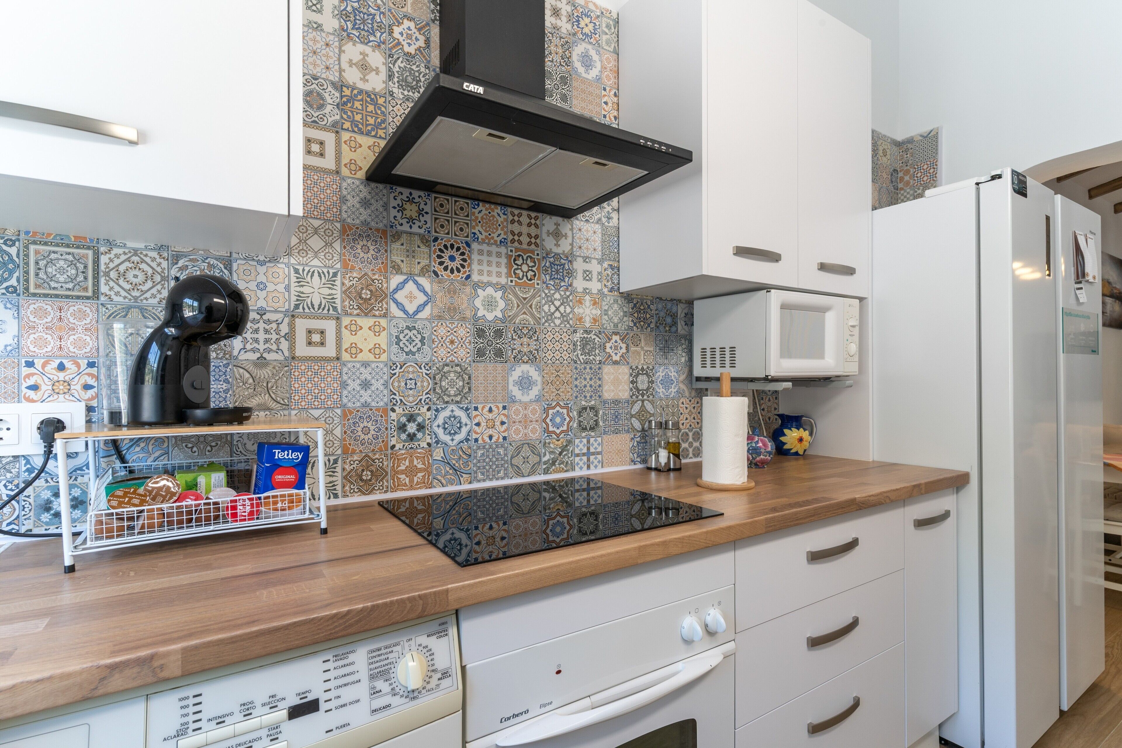 A modern kitchen with a patterned backsplash, a black range hood, a microwave, and a dishwasher.