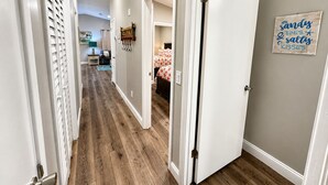 Un pasillo con suelo de madera, paredes blancas y una puerta que da a un dormitorio con cama.