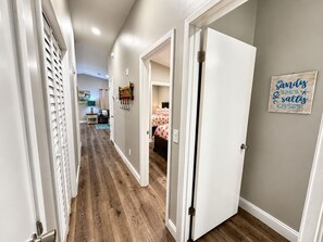 A hallway with wooden flooring, white walls, and a door leading to a bedroom with a bed. - Coastal Boaters' Dream 3-bedroom house near public boat ramp - Sleeps 8 (Panama City Beach)