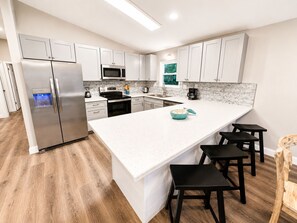 A modern kitchen with white cabinetry, stainless steel appliances, a large island with bar stools, and a wooden floor. - Coastal Boaters' Dream 3-bedroom house near public boat ramp - Sleeps 8 (Panama City Beach)