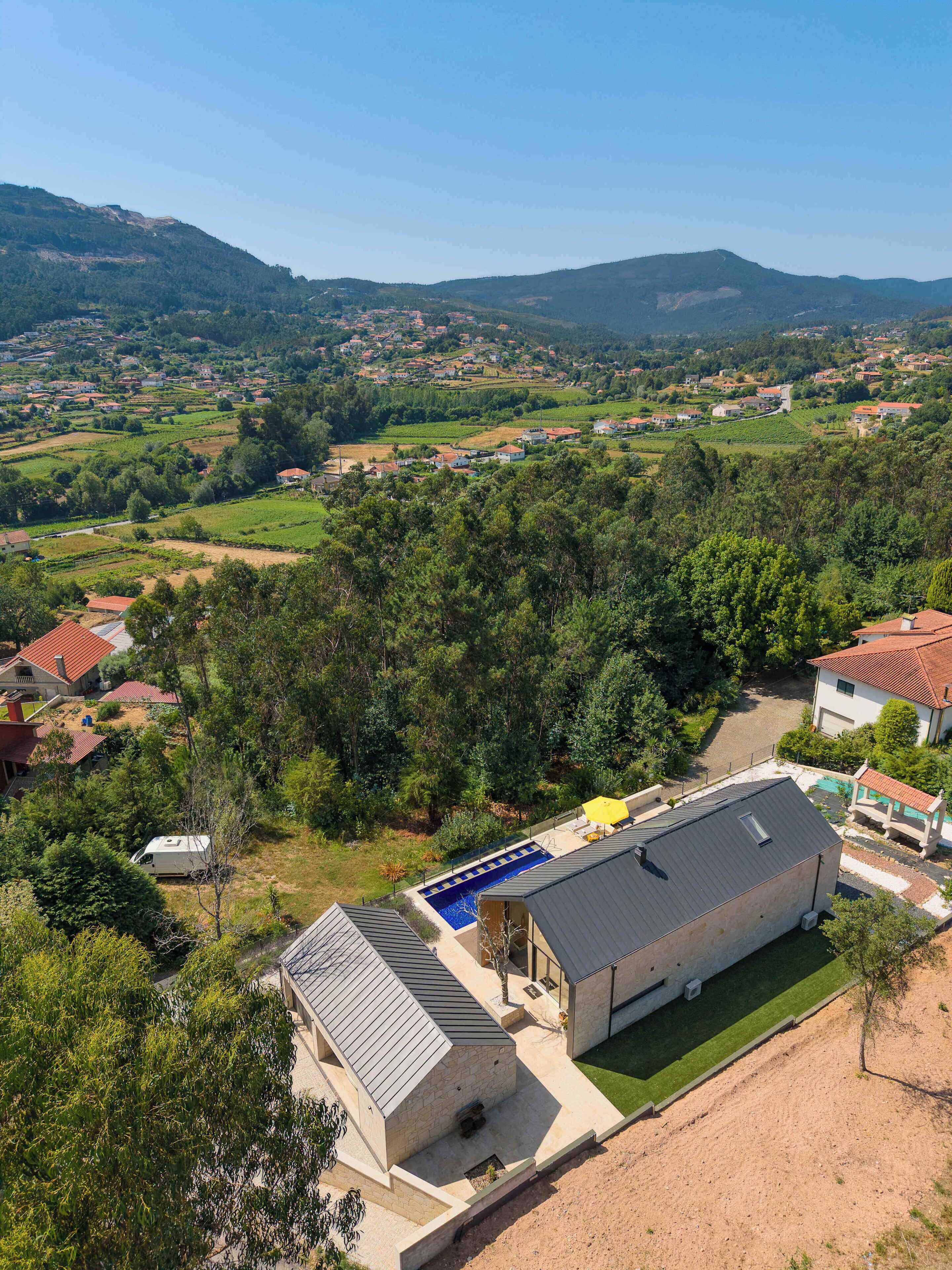 Zona residencial con una casa grande que cuenta con una piscina, rodeada de vegetación y colinas al fondo.