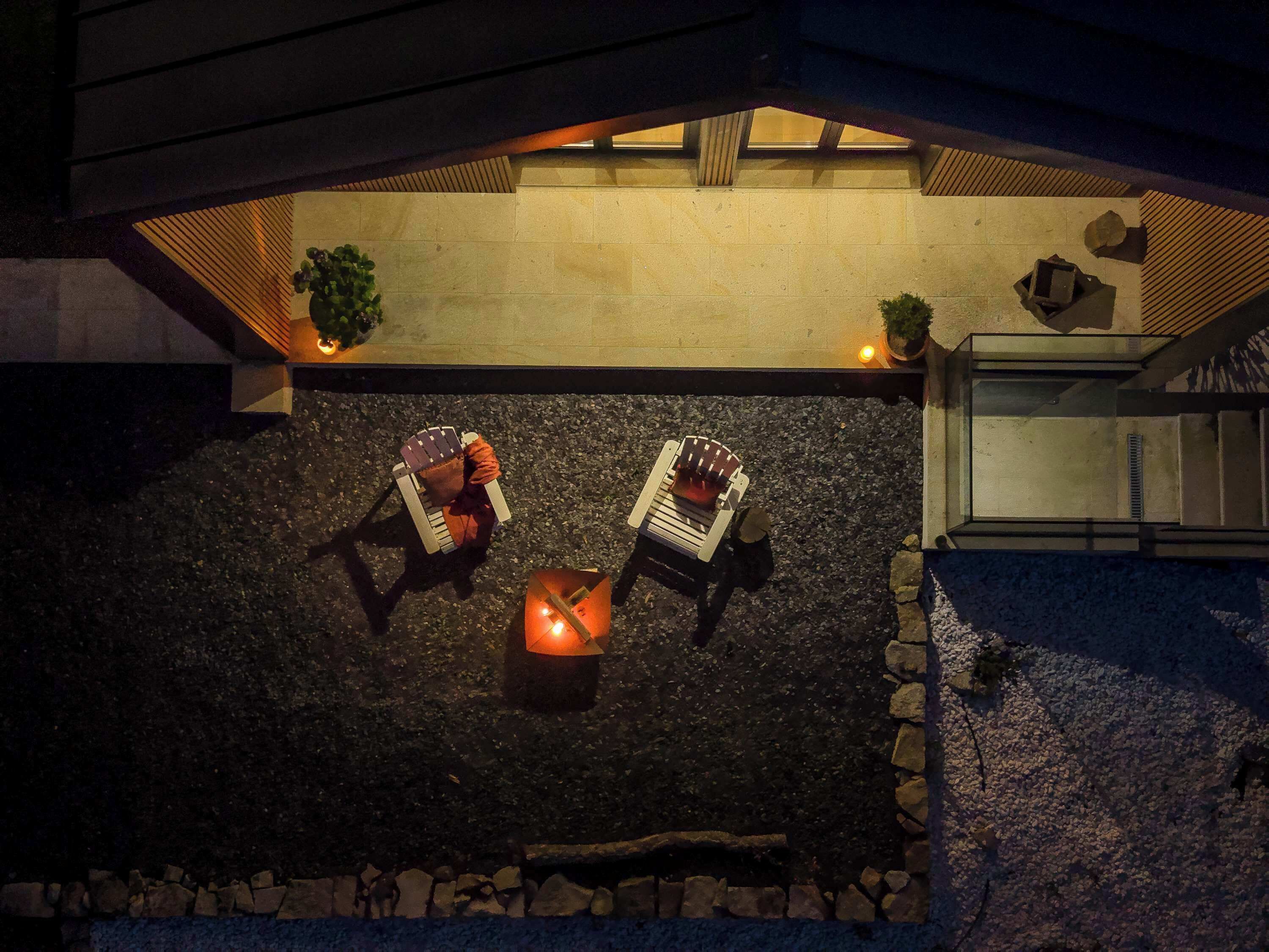 An outdoor seating area with two chairs and a fire pit, surrounded by a stone wall and a building with a sloped roof.