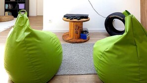 Ein modernes Wohnzimmer mit einem flachbildfernseher an der Wand, einem hölzernen Couchtisch mit elektronischen Geräten und zwei grünen Sitzsäcken.