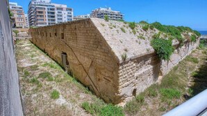 A stone fortification with a steep, grassy slope and a clear view of the sea in the background. - Modern 1BR in Fort Cambridge, Sliema | AC & WIFI (Sliema)