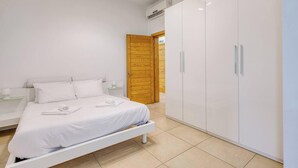 A bedroom with a bed, a nightstand, a wardrobe, and a wooden door. - Modern 1BR in Fort Cambridge, Sliema | AC & WIFI (Sliema)