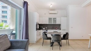 A modern apartment with a dining area, kitchen, and a balcony with a view of buildings. - Modern 1BR in Fort Cambridge, Sliema | AC & WIFI (Sliema)