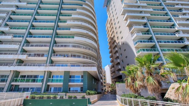 A high-rise hotel with multiple balconies, a central stairway, and palm trees. - Modern 1BR in Fort Cambridge, Sliema | AC & WIFI (Sliema)