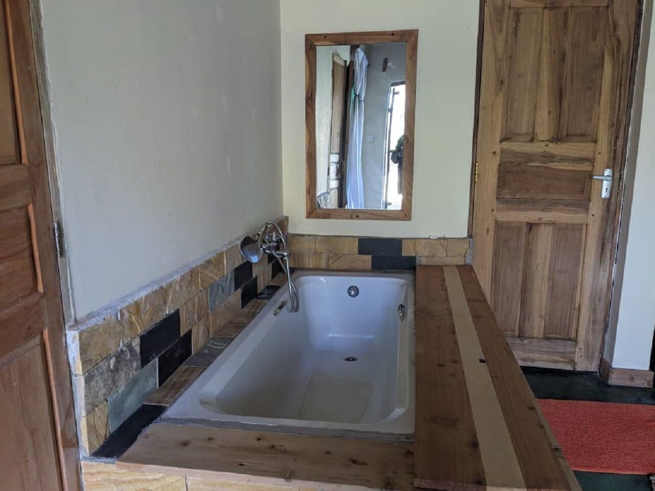 Een badkamer met een badkuip, een houten deur en een spiegel.