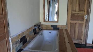 Een badkamer met een badkuip, een houten deur en een spiegel.