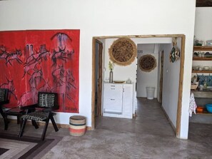 A room with a red abstract painting, a white cabinet, and a woven wall hanging. - Giraffe Gallery Home-Josmac Tours & Arts (Arusha)