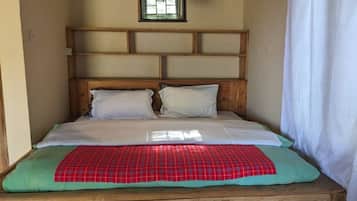 A single bed with a wooden headboard, a red and green checkered blanket, and white pillows.