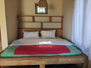 Una cama individual con cabecera de madera, una colcha de cuadros rojos y verdes, y almohadas blancas.