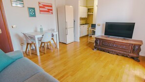 Ein Wohnzimmer mit einer Couch, einem Esstisch mit Stühlen, einem Fernseher auf einer Holzkommode, einem Kühlschrank und Küchenschränken.