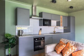 Eine kompakte Küche mit einer Bosch-Mikrowelle, Backofen und Geschirrspüler, einem Waschbecken mit Goldarmatur und einem Blumentopf.
