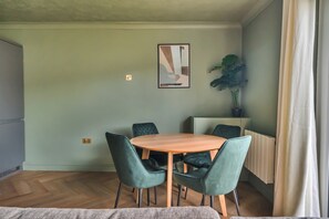 A dining area with a round wooden table and four chairs, a potted plant, and a painting on the wall. - 2 Bed Apartment Sleeps 4 - Pets Welcome (St Ives)