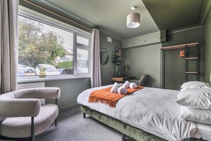 A hotel room with a bed, a chair, a window with curtains, a bedside table, and a mirror. - 2 Bed Apartment Sleeps 4 - Pets Welcome (St Ives)