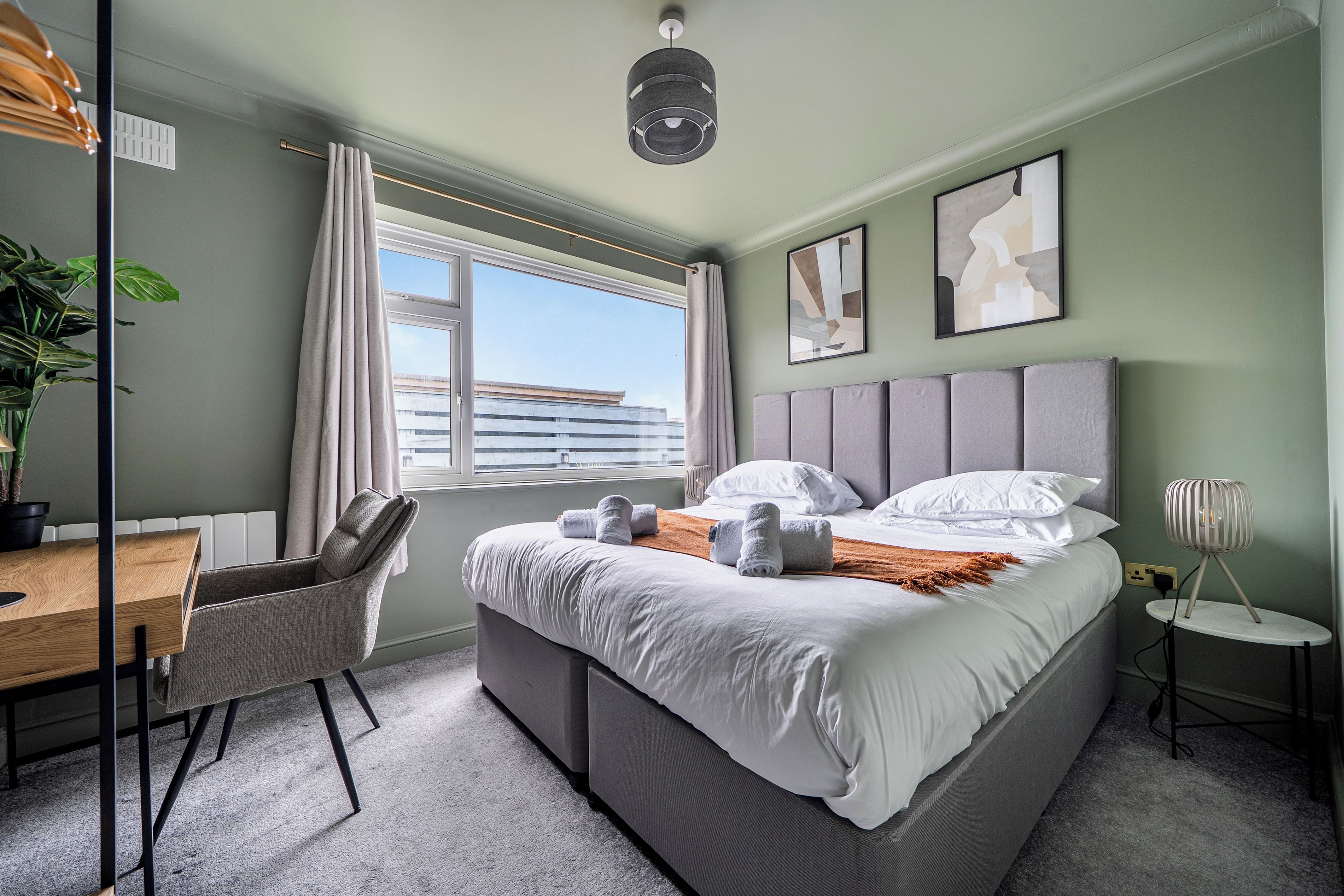 A modern hotel room with a large bed, a desk, and a window with curtains.