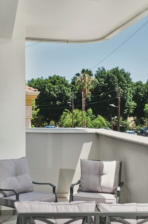 A balcony with two chairs and a table, overlooking a residential area with trees and parked cars. - Modern 1BR W/Balcony in Central Nicosia (Nicosia)