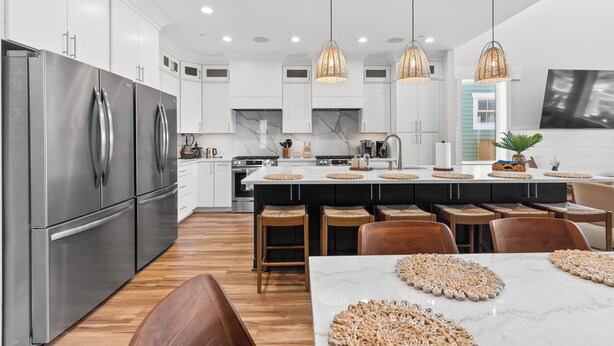 A modern kitchen with stainless steel appliances, a central island with stools, pendant lighting, and a view of the outside. - Luxury Oceanfront, Pool, Elevator, Volleyball (Oak Island)