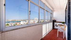 Un balcón con vista a la ciudad, lavadora y una mesita con una planta.