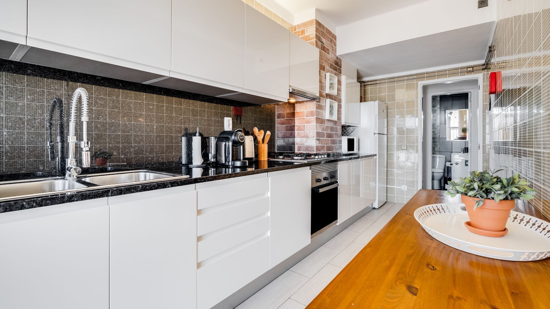 Een moderne keuken met witte kasten, een zwart aanrecht en een tegelwand.