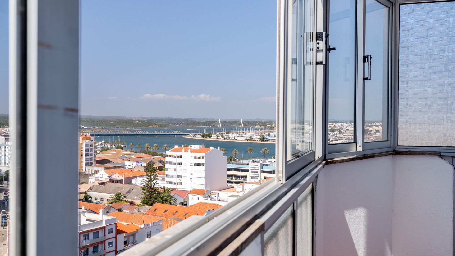 A view from a window overlooking a coastal city with buildings, a bridge, and a marina.