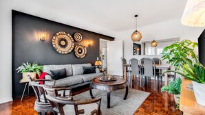 Una sala de estar moderna con una pared oscura, un sofá gris, sillas de madera, una mesa de centro y decoración en la pared.