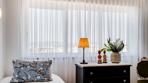 Un dormitorio con una cama, una mesita de noche, una lámpara, adornos y cortinas translúcidas.