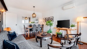 Una sala de estar moderna con un sofá, una mesa de comedor, sillas, una mesa de centro, un televisor y una planta en maceta.