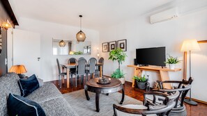 Ein modernes Wohnzimmer mit einer Couch, einem Esstisch, Stühlen, einem Couchtisch, einem Fernseher und einer Topfpflanze.