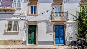 Um edifício com duas portas, uma verde e outra azul, e uma varanda com grade de ferro forjado.