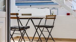 A balcony with two foldable chairs and a small table, a white wall, and a blue and white building in the background. - Rooftop Terrace in Tavira by LovelyStay (Tavira)
