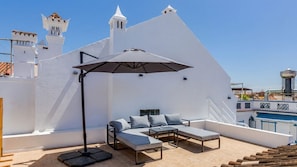 Eine Dachterrasse mit einem weißen Gebäude, einem Pool und einer Sitzecke mit Tisch und Stühlen.