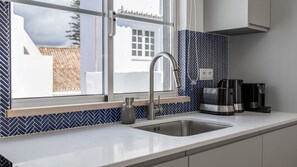 Cozinha moderna com pia de aço inoxidável, janela com vista para edifícios e cafeteira no balcão.