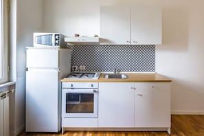 Cocina compacta con microondas, refrigerador, horno, estufa a gas, lavaplatos y gabinetes blancos.
