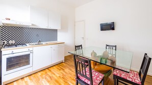 Una cocina funcional con estufa, horno y un pequeño comedor con mesa de vidrio y sillas.