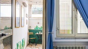 Una habitación con ventana, un radiador, una mesa con sillas e imágenes enmarcadas en la pared.