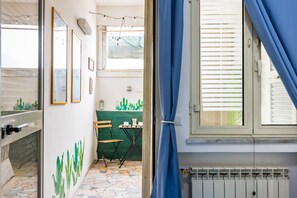 Ein Zimmer mit Fenster, Heizkörper, Tisch mit Stühlen und Bildern in Rahmen an der Wand.
