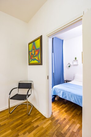 Una habitación con cama, una silla, un cuadro y una cortina azul.