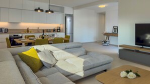 Uma sala de estar moderna com um sofá cinzento, uma mesa de centro de madeira e uma TV sobre um móvel de madeira.